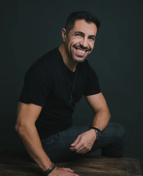 Fernando Souza smiling, seated at a wooden table in the studio.